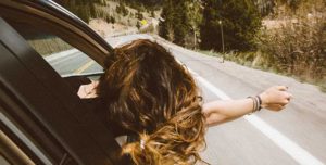 girls hangs out of car window with wind in her hair